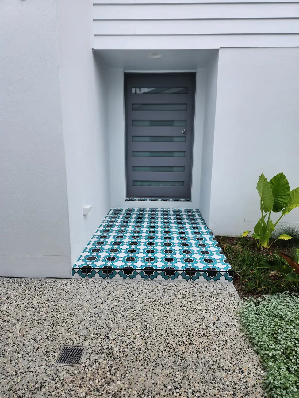 Front entry step tiled in a teal and white patterned tile beside a garden