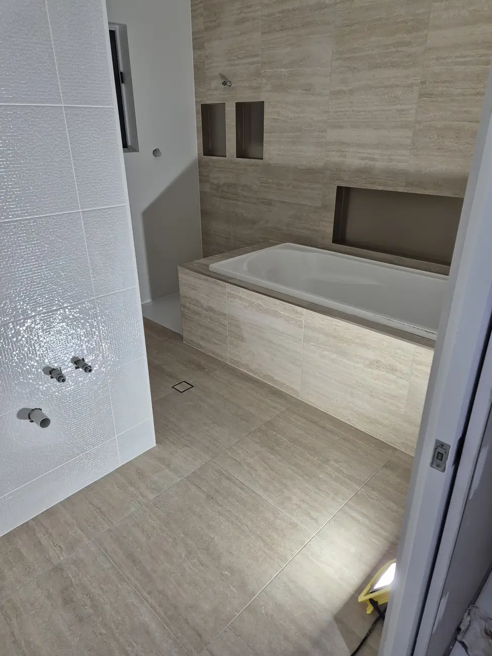 Bathroom with timber-look floor tiles, a tiled bath surround with niche and white gloss wall tiles