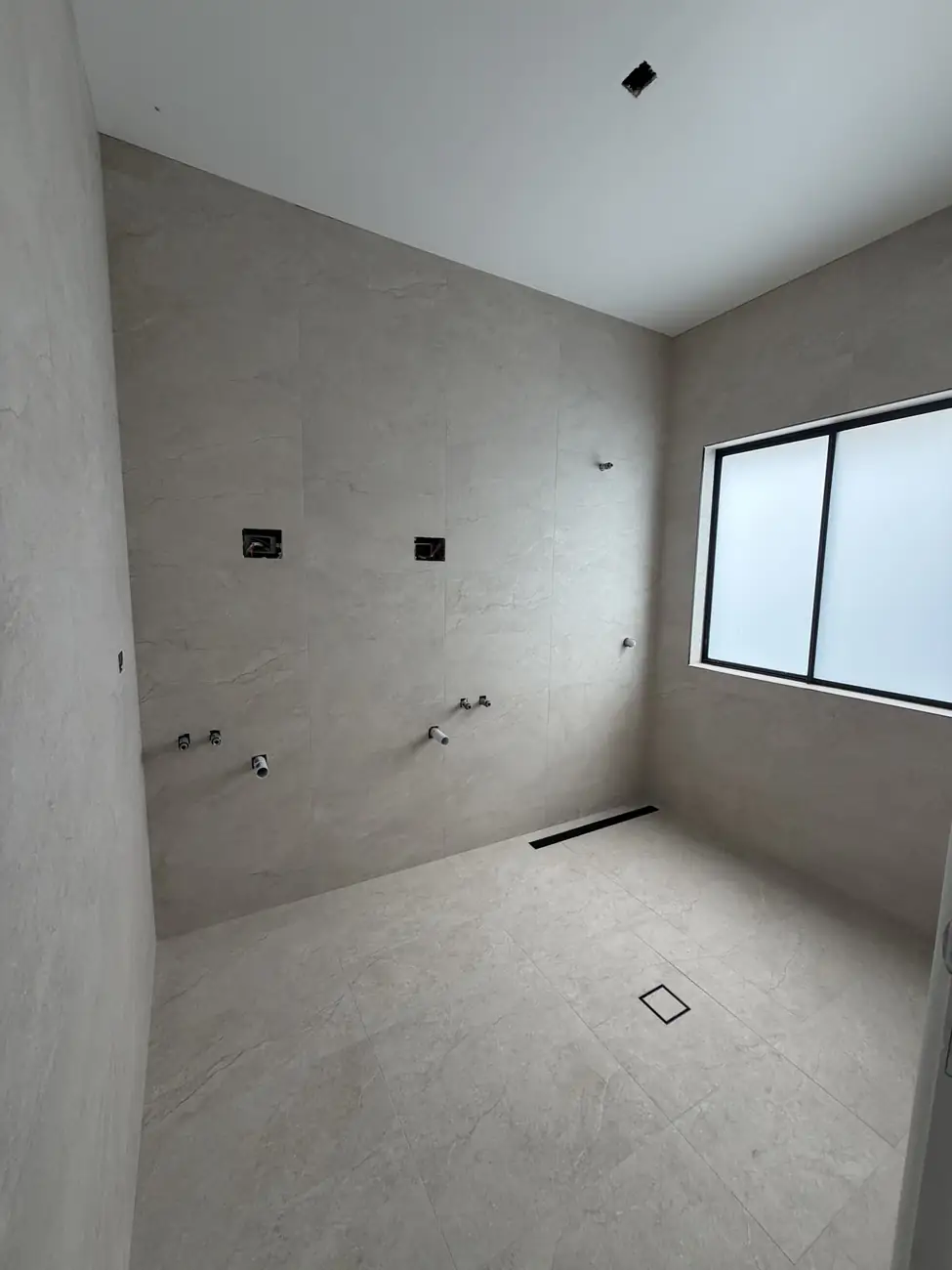 Tiled bathroom before fit-off, with a linear drain along the wall and a square floor waste