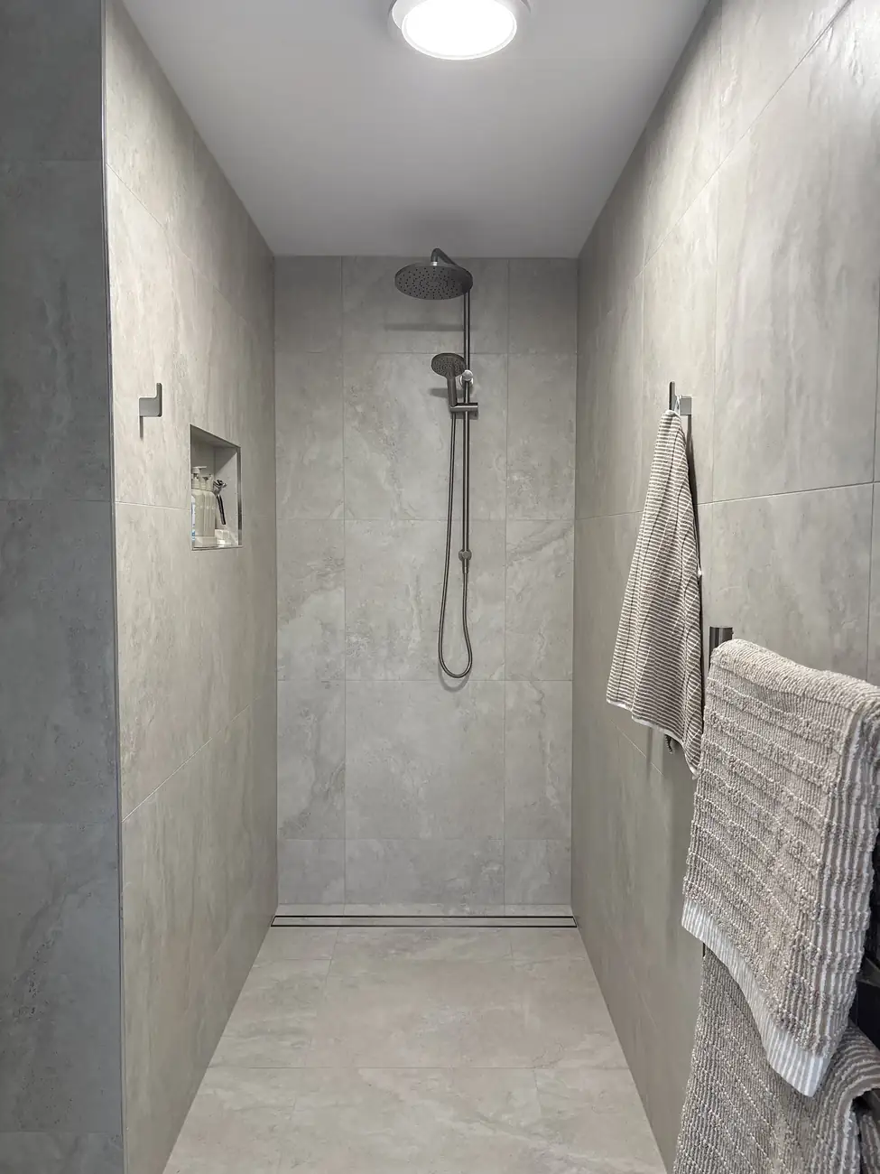 Walk-in shower tiled in large-format grey tiles with a recessed niche