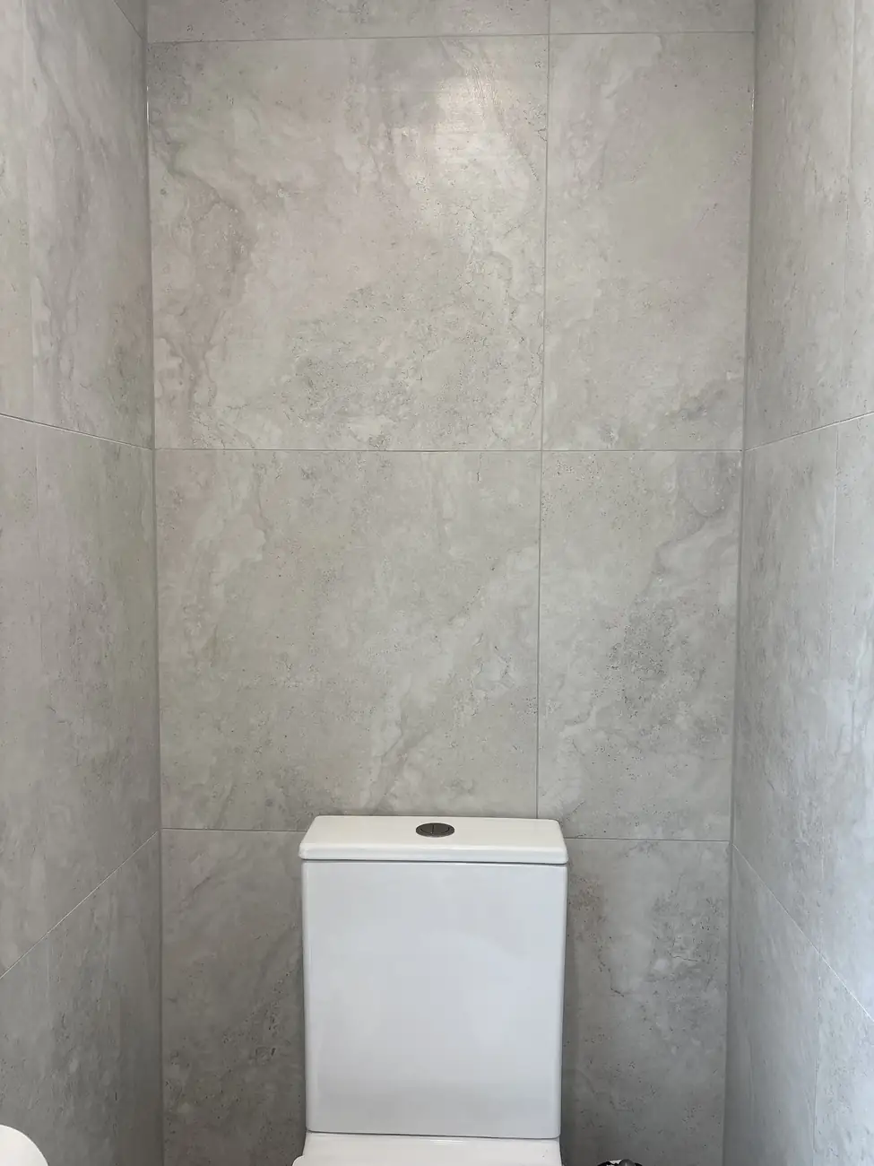 Large-format grey wall tiles running floor to ceiling behind a toilet