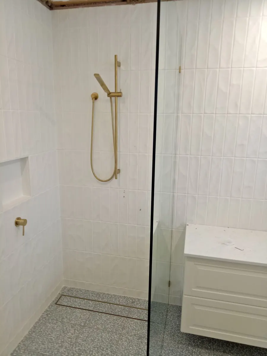 White wall tiles in a shower with brushed-gold fittings